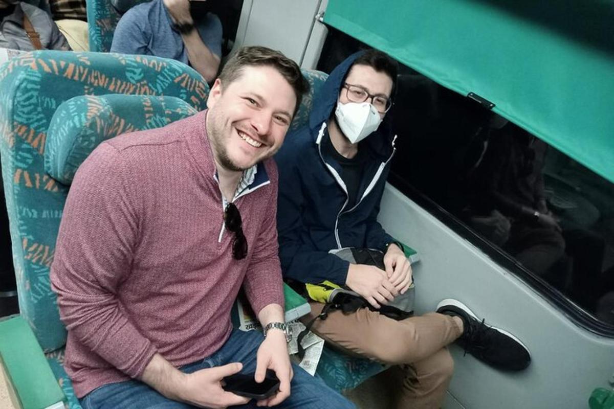 two men sitting on a train wearing a mask
