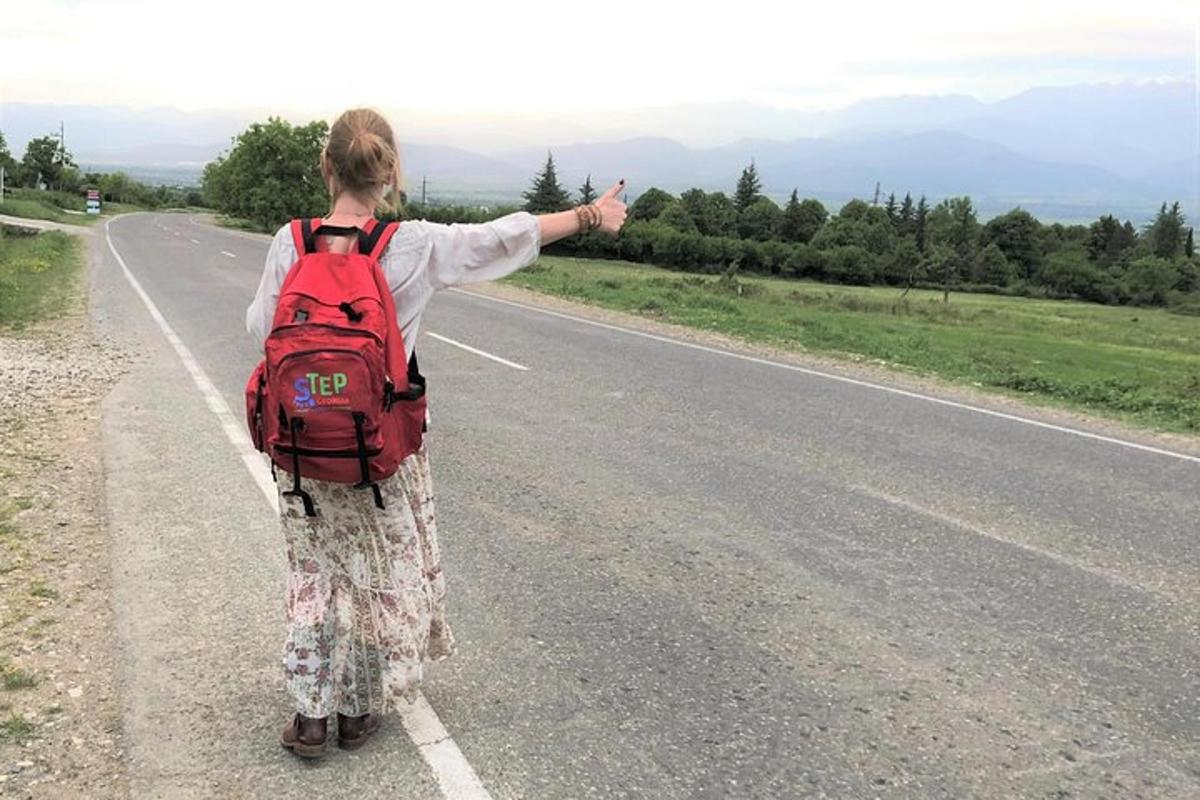 una donna con uno zaino in piedi su una strada con il braccio teso