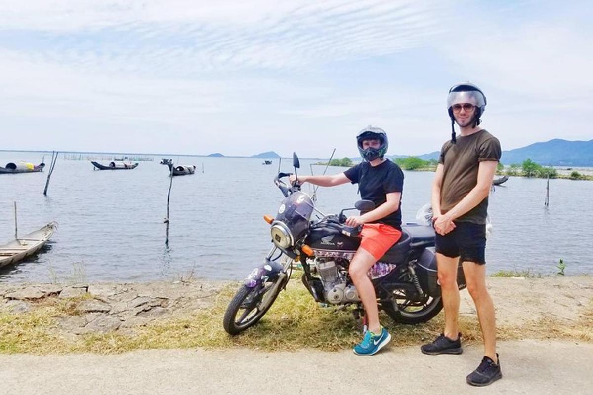 Dos hombres de pie junto a una motocicleta junto al agua.