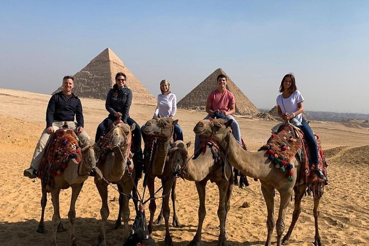 Skupina lidí jedoucích na velbloudech před pyramidami