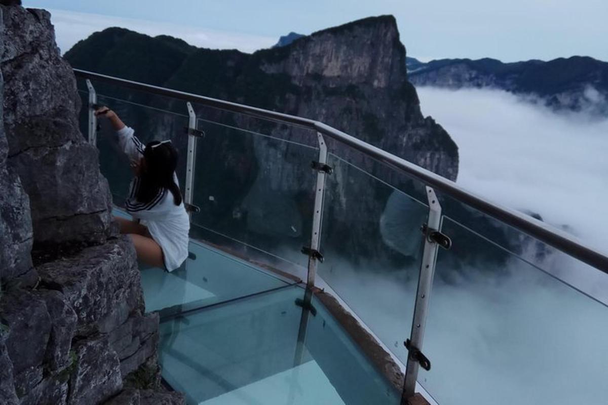 a woman sitting on a glass ledge looking at the mountains