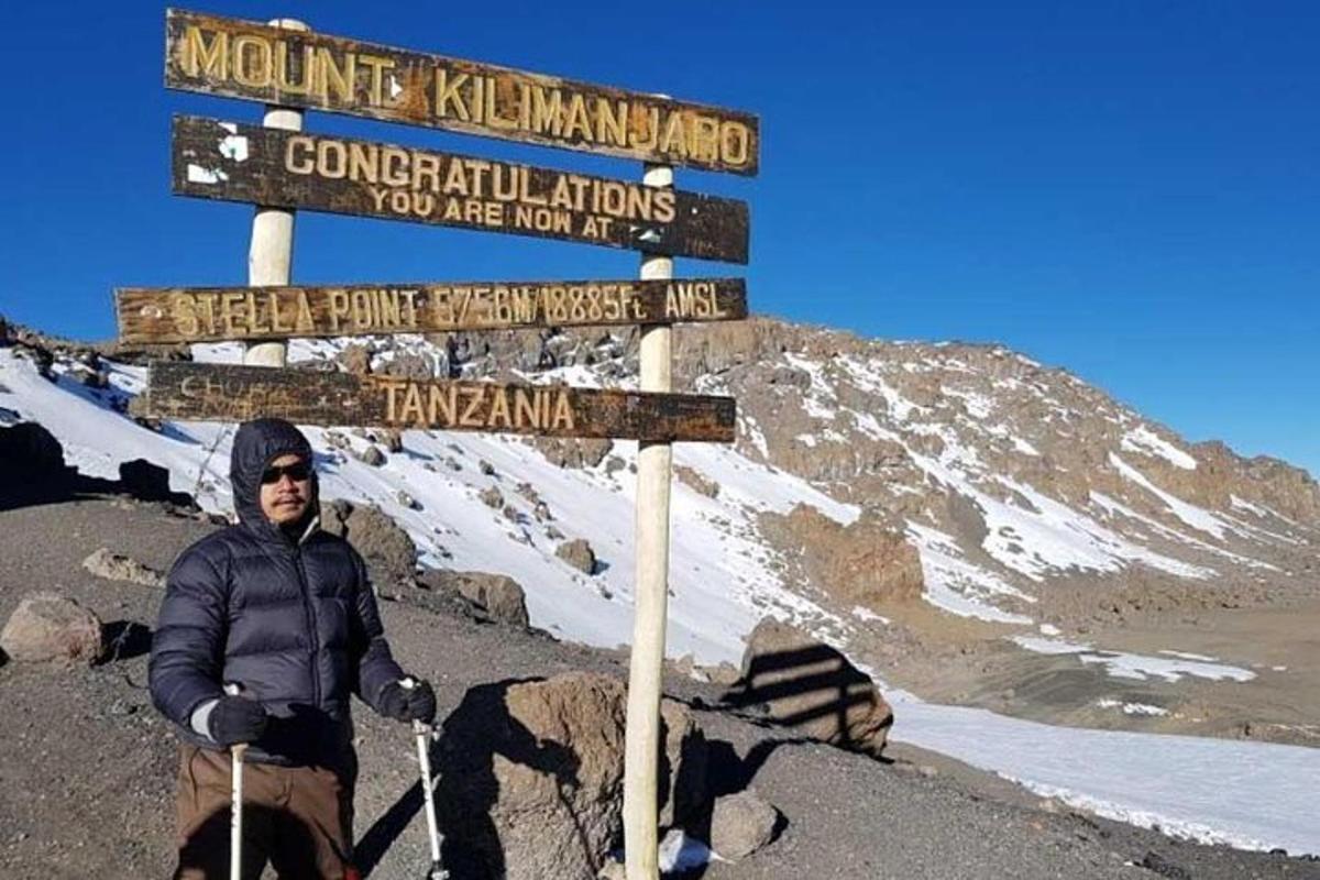 um homem parado ao lado de uma placa em uma montanha