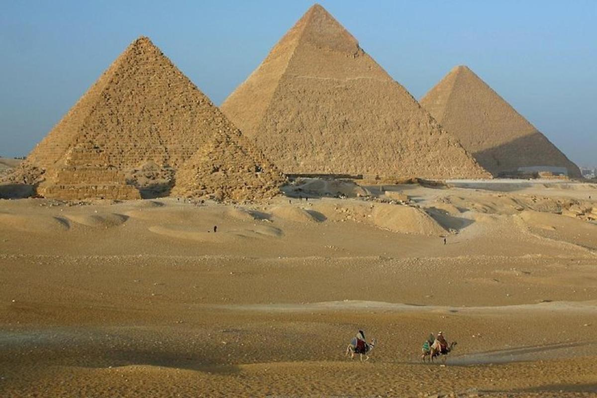 dva lidé jedoucí na koních před pyramidami