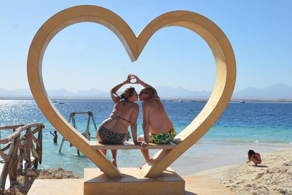 duas mulheres sentadas em uma escultura de coração na praia