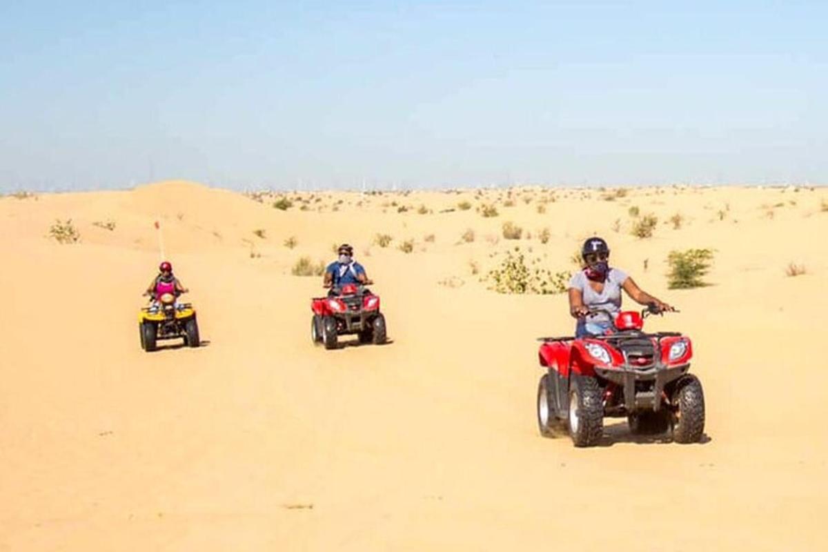 three people riding on atvs in the desert