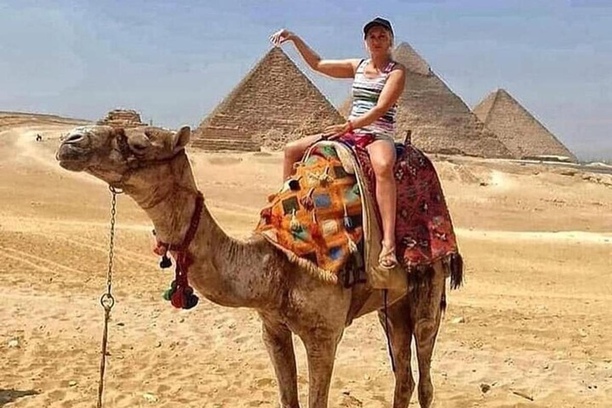 žena jedoucí na velbloudovi před pyramidami