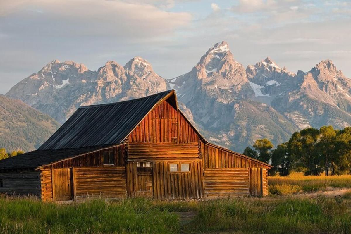 un vecchio fienile di legno in un campo con le montagne sullo sfondo