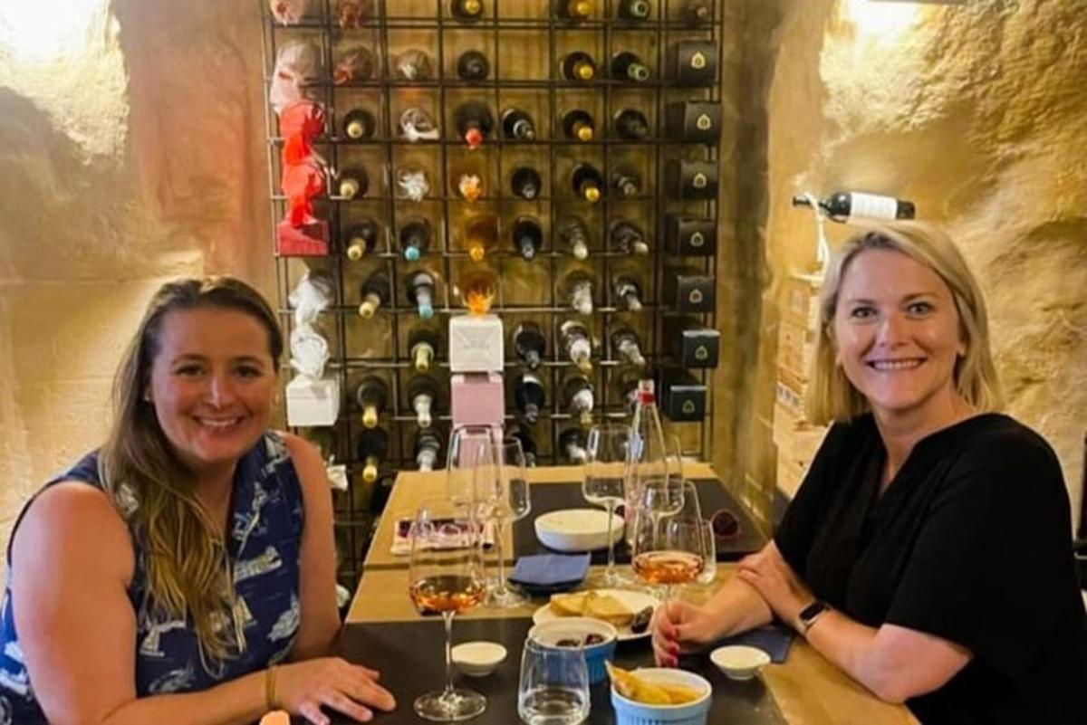 two women sitting at a table with wine bottles