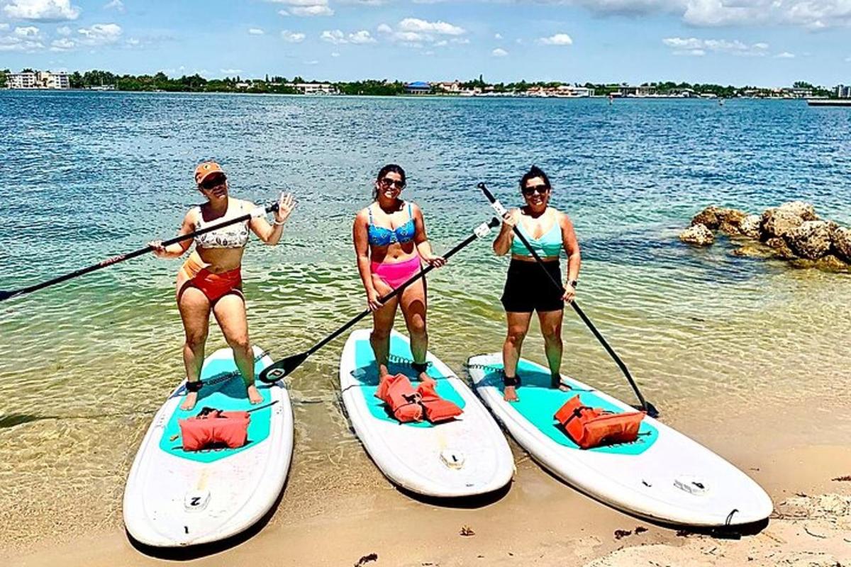Tri ženske stojijo na deskah za veslanje na plaži