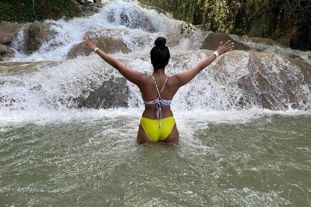 a woman standing in the water in front of a waterfall