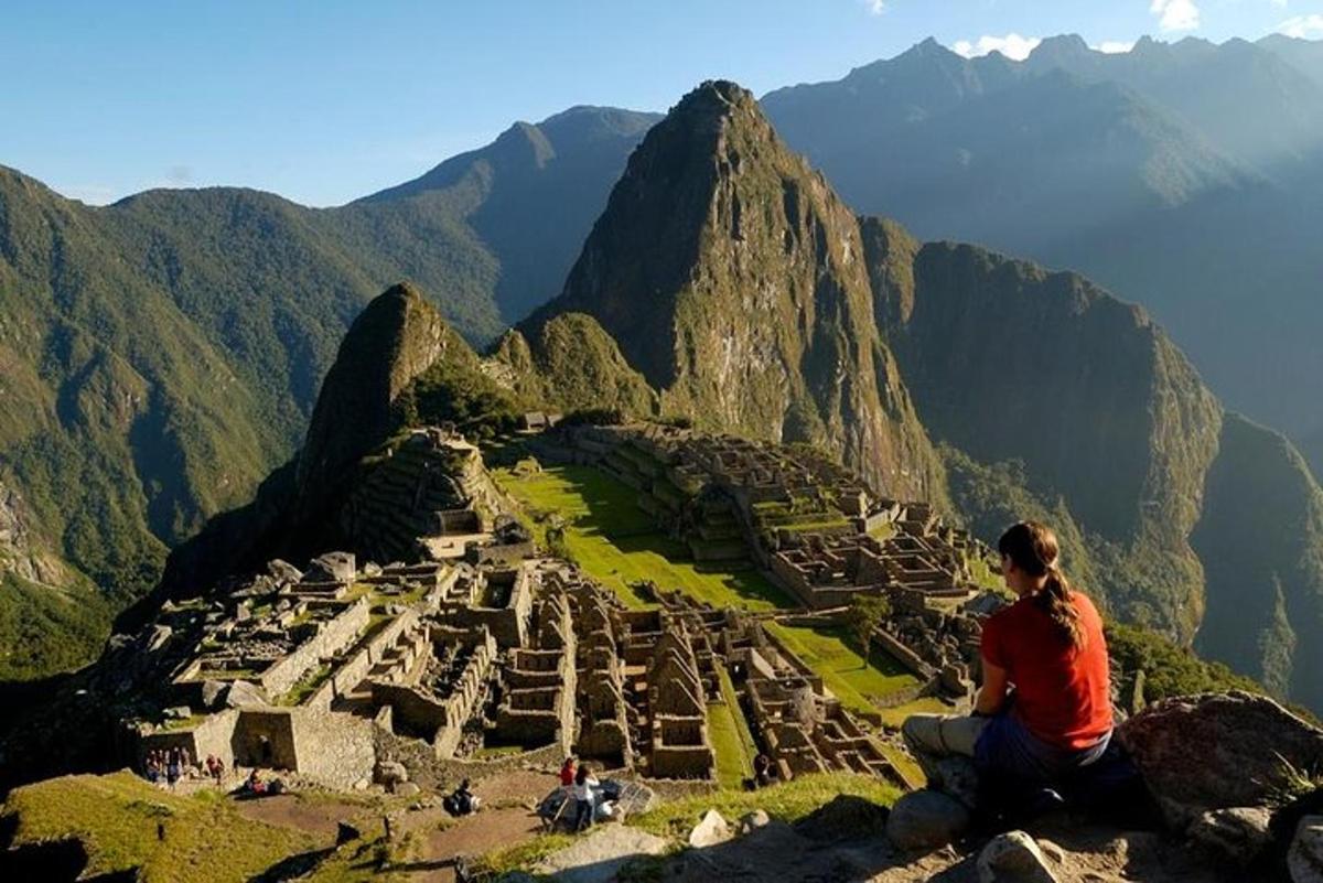 Un hombre sentado en el borde de una montaña con vistas a una ciudad.