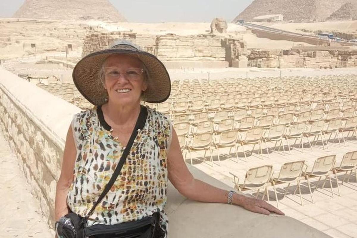 žena v klobouku sedící na zdi před pyramidami