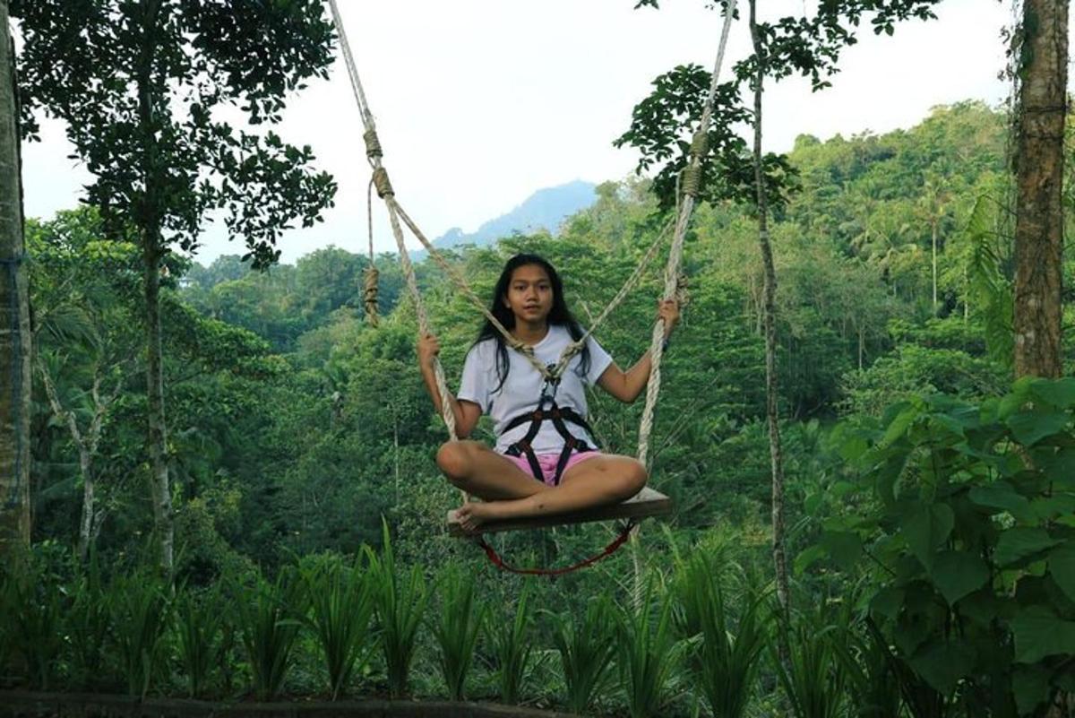a girl sitting on a rope swing in the jungle