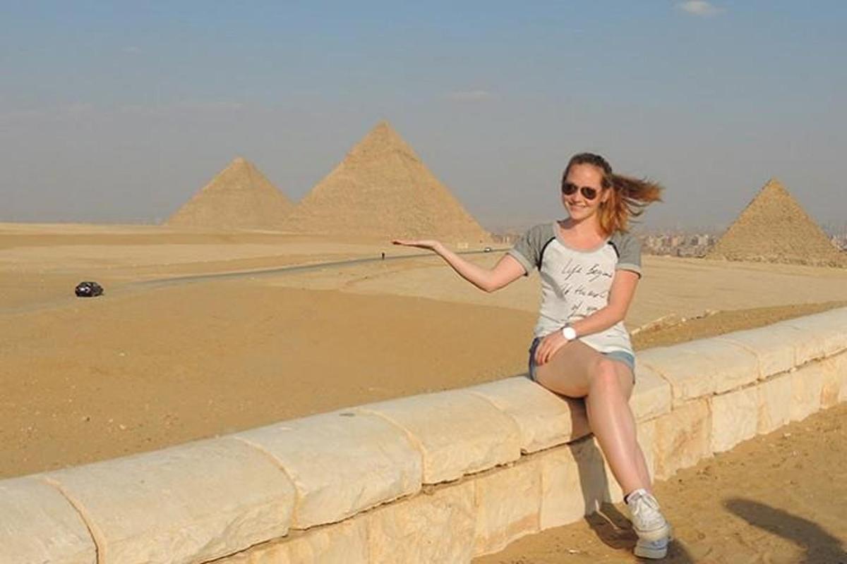 Una mujer sentada en un muro frente a las pirámides.