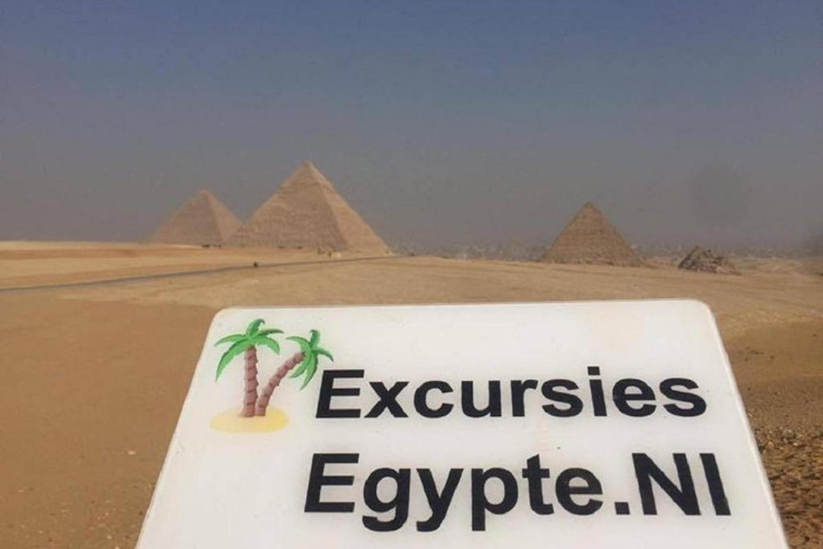 Un cartel en el desierto con las pirámides al fondo.