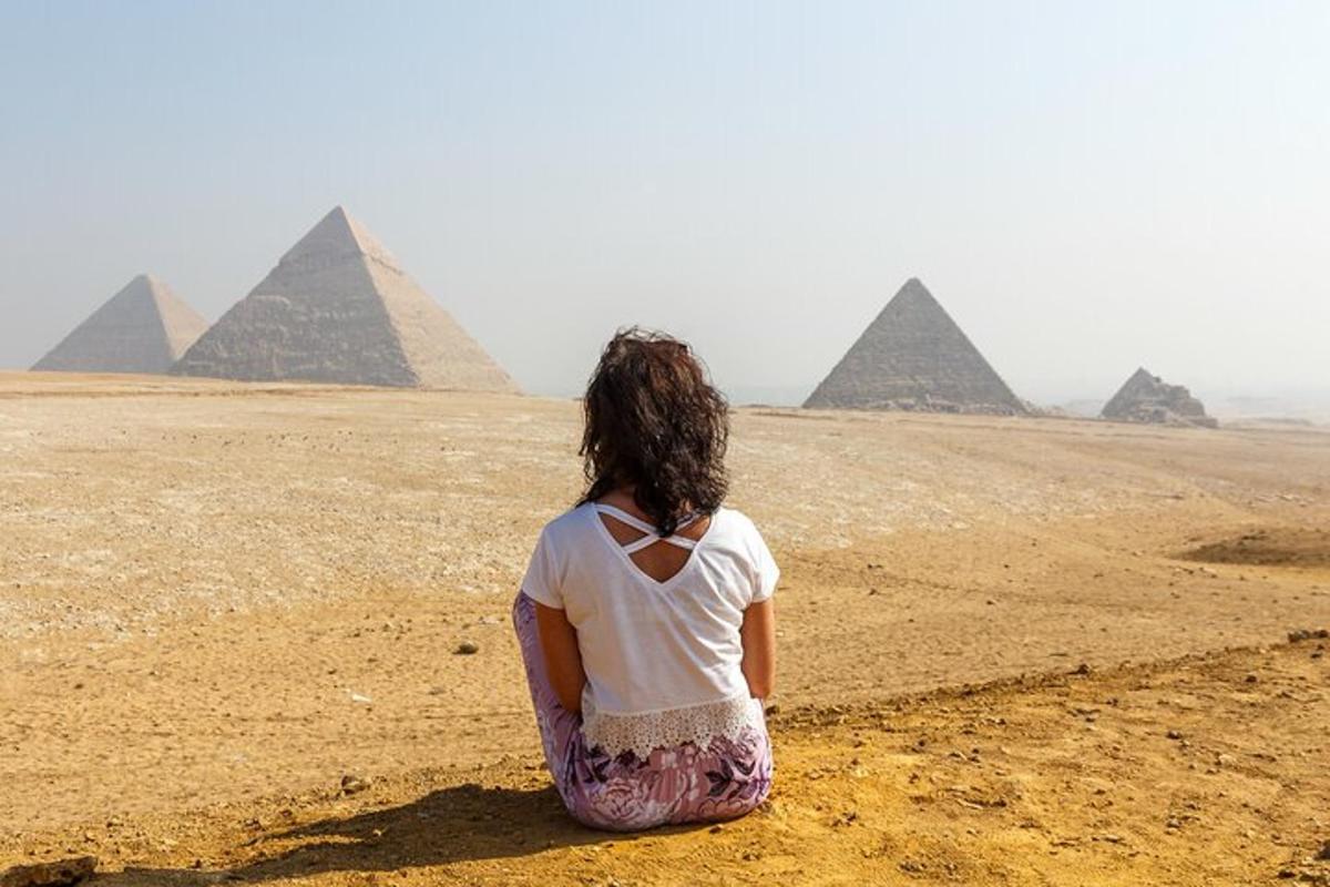 en kvinne som sitter i ørkenen og ser på pyramidene