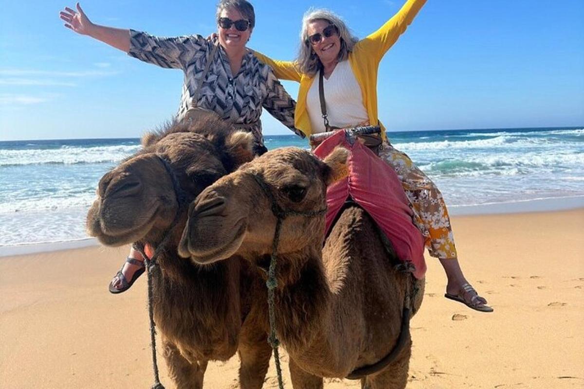two people riding on a camel on the beach