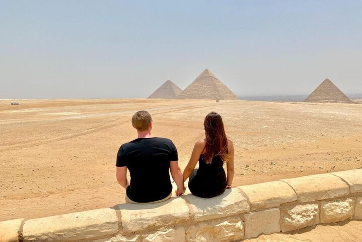 Moški in ženska sedita na zidu in gledata piramide