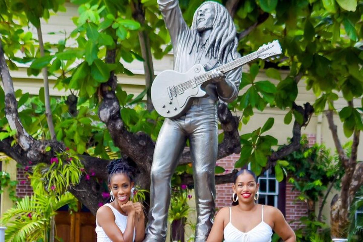 two women pose in front of a statue of a guitar player