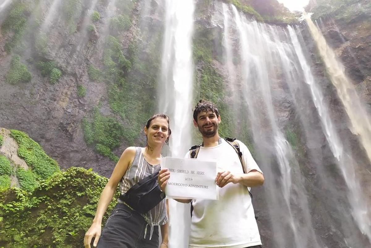 a man and woman holding a sign in front of a waterfall