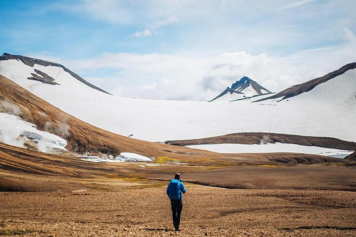 a man walking through a field in front of a snow covered mountain