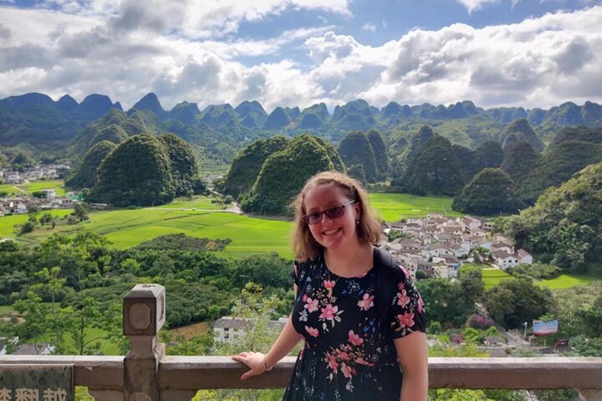 a woman standing on a fence overlooking a valley
