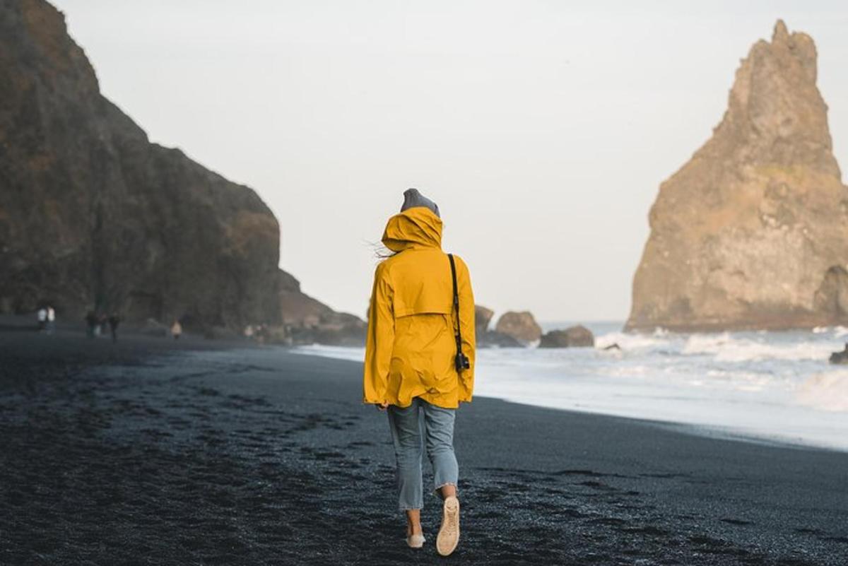 eine Frau, die mit einer gelben Jacke am Strand spazieren geht