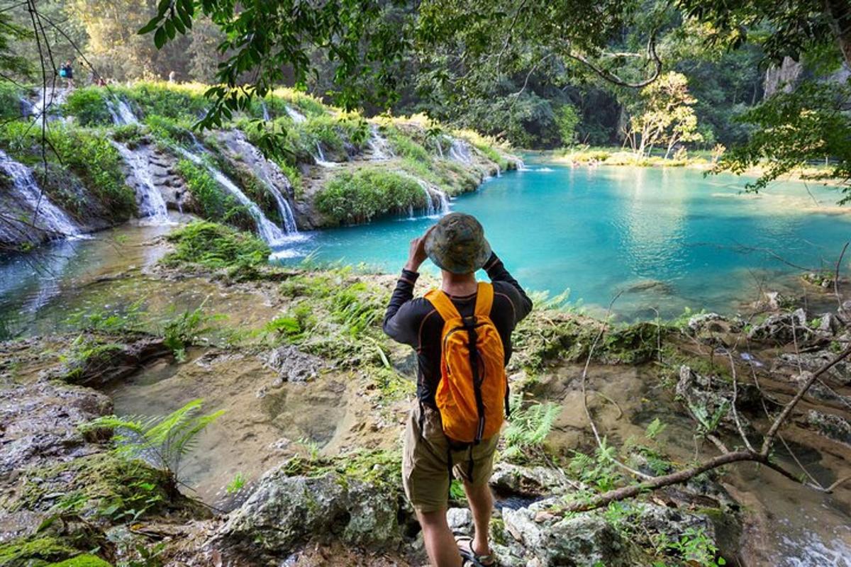 Un hombre con una mochila naranja mirando un río.