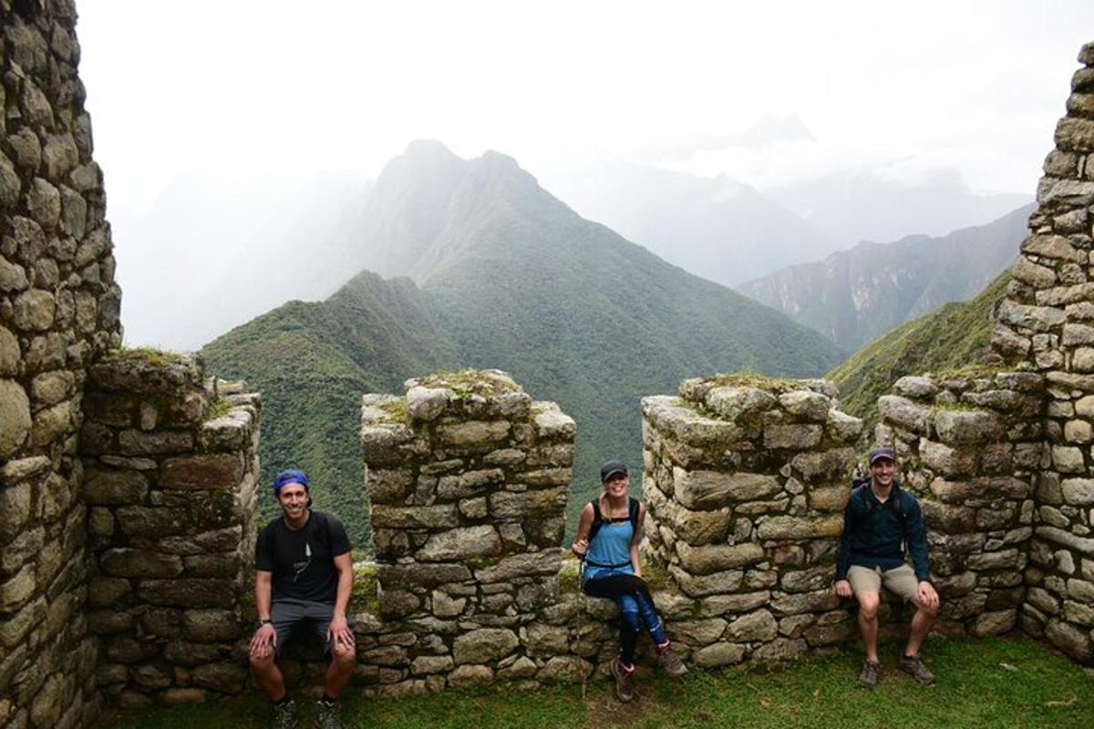 tre persone sedute tra le rovine di un muro di pietra con le montagne sullo sfondo