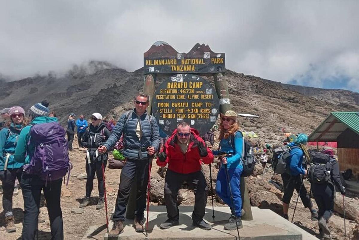 sekelompok orang berdiri di samping tanda di gunung