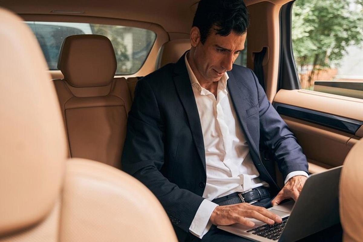 um homem sentado no banco de trás de um carro usando um laptop