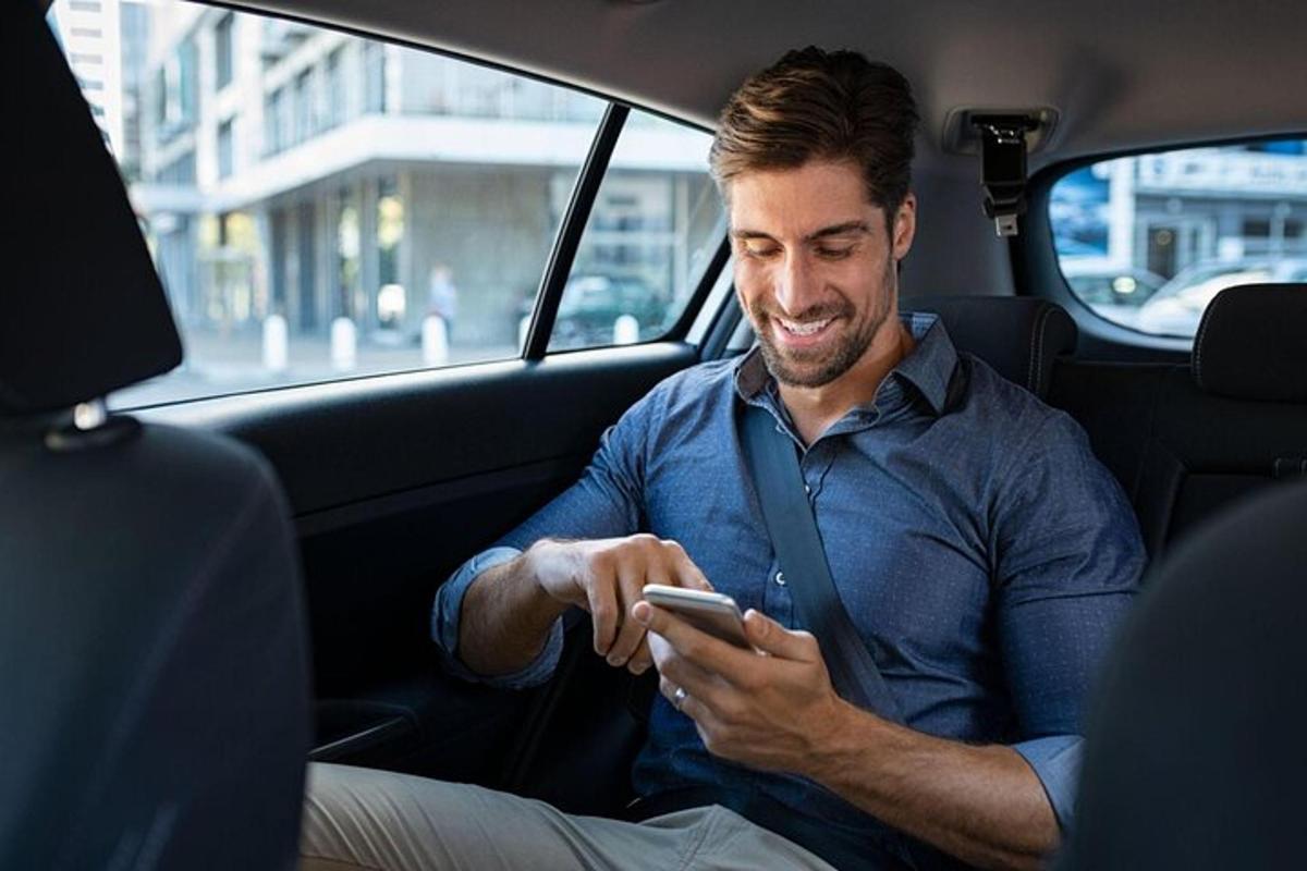 seorang pria duduk di kursi belakang mobil sambil melihat ponselnya