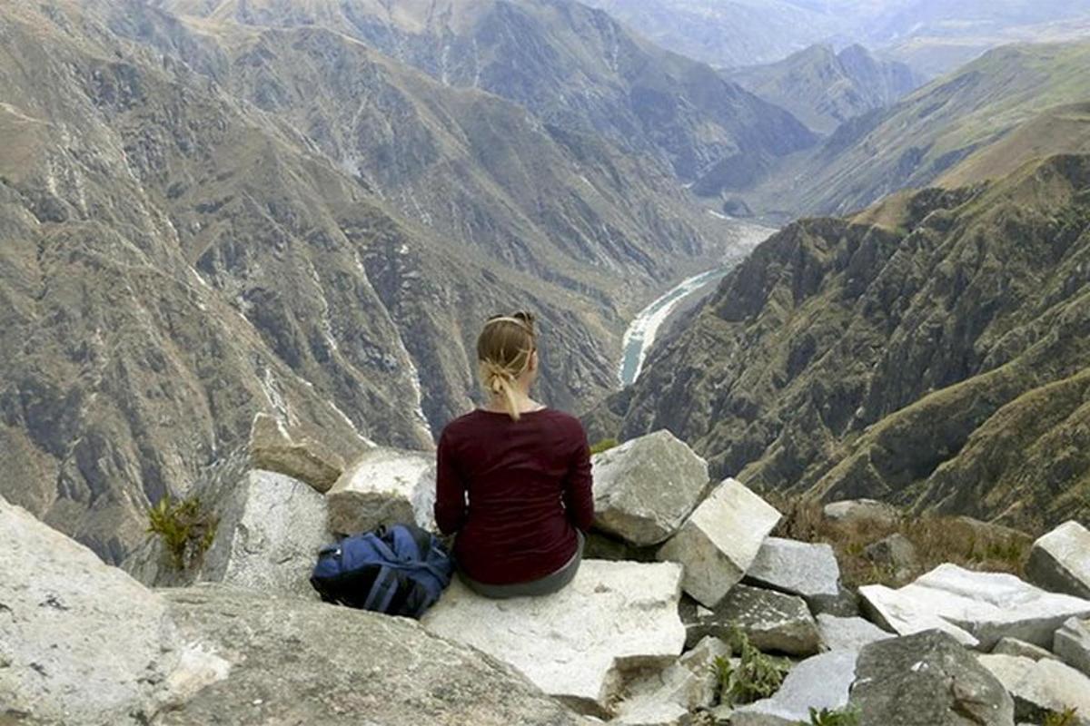 Una mujer sentada en una roca mirando un valle de montaña