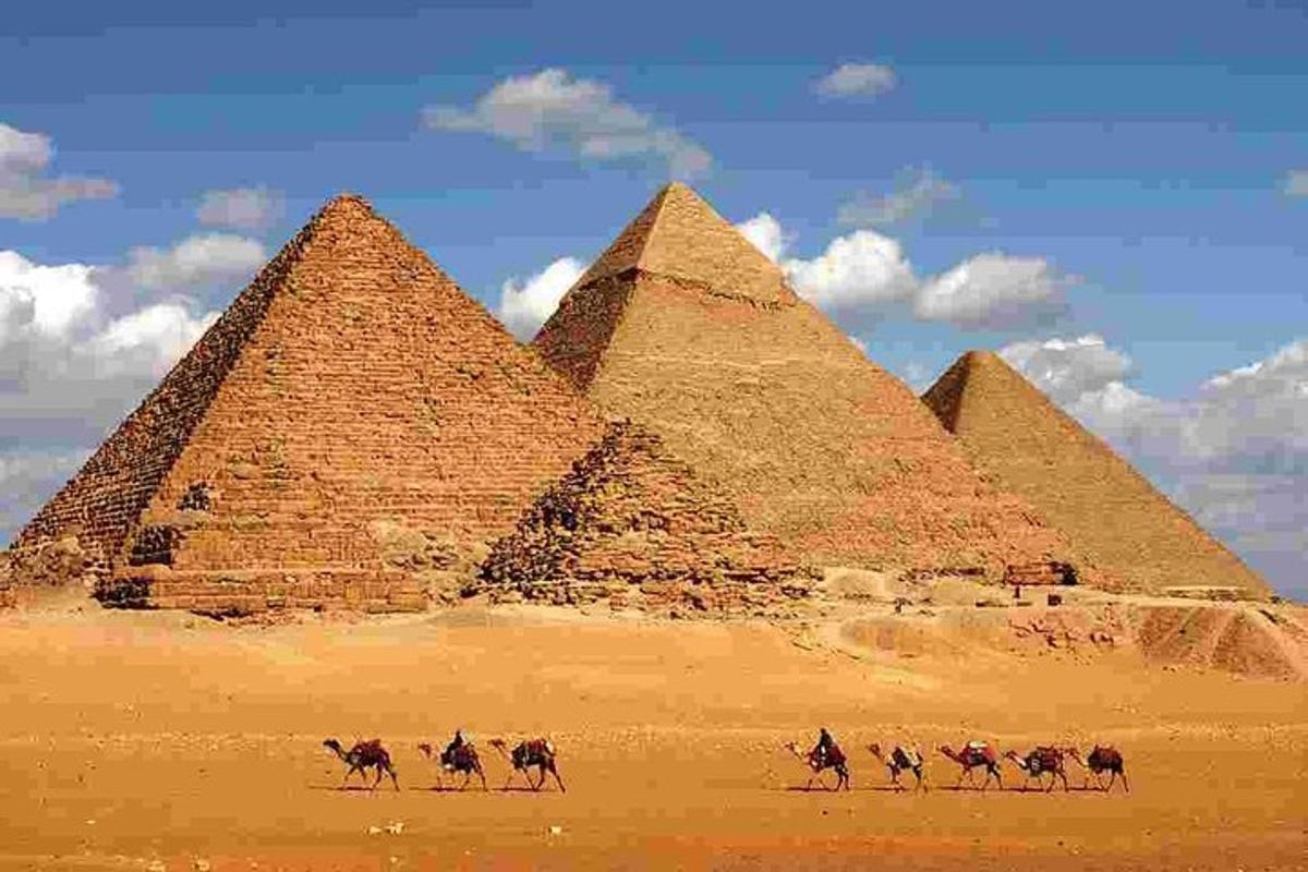 eine Gruppe von Menschen, die vor Pyramiden auf Kamelen reiten