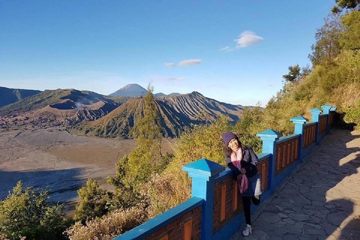 seorang wanita duduk di atas pagar sambil melihat pergunungan