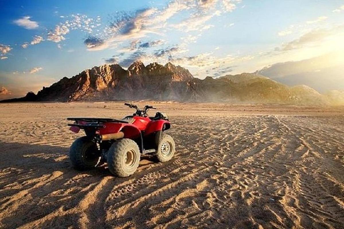 un quad vermell aparcat al desert amb una muntanya al fons