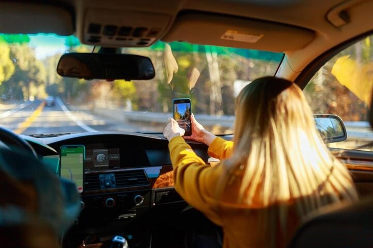 ženska, ki v avtu drži mobilni telefon
