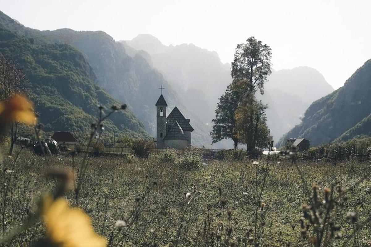 a church in the middle of a field with mountains