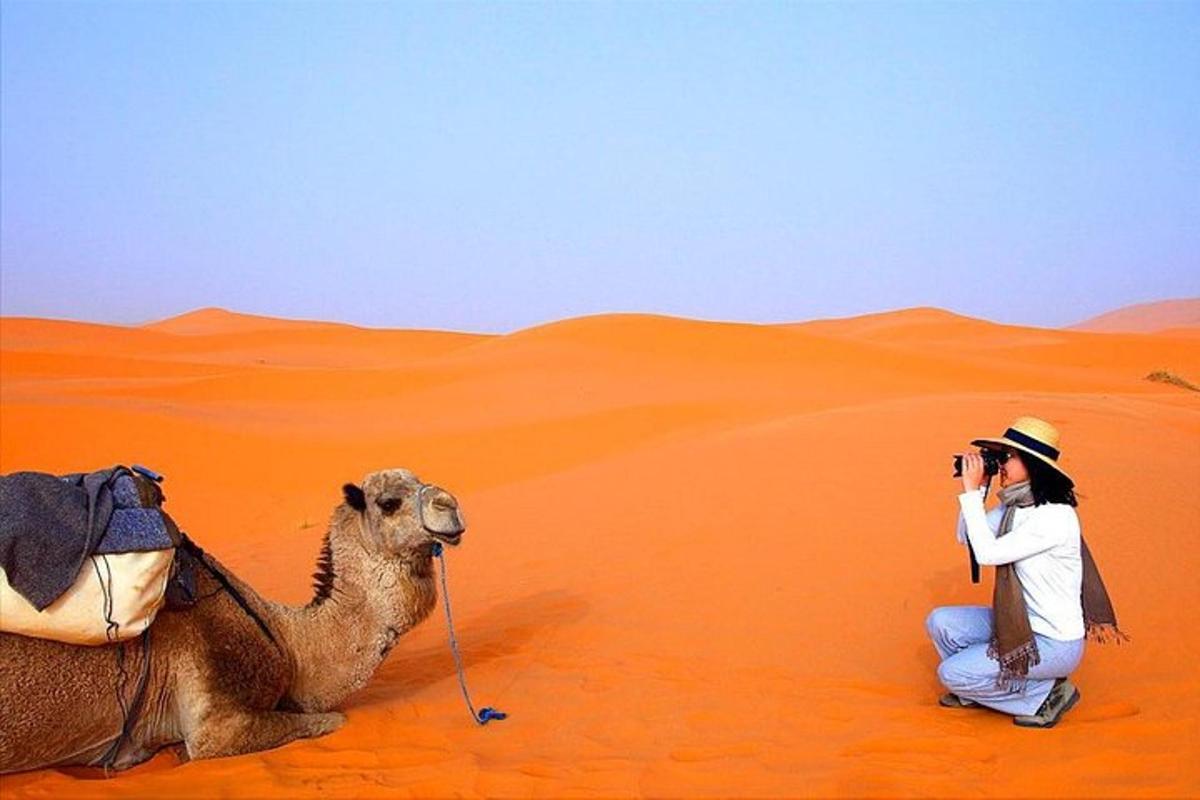 un home fent una foto d'un camell al desert