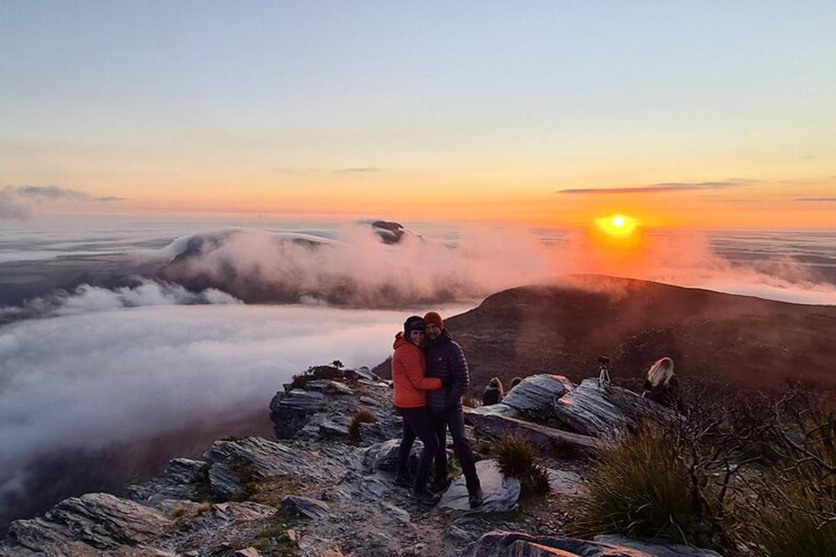 Dos personas de pie en la cima de una montaña al atardecer