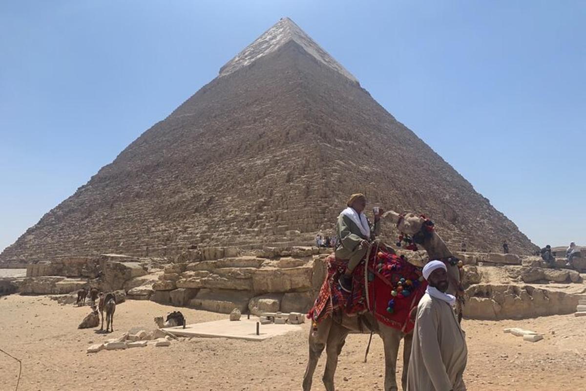 Skupina lidí jedoucích na velbloudovi před pyramidou