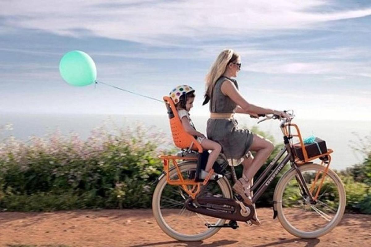 seorang wanita menunggang basikal dengan seorang kanak-kanak memegang belon hijau