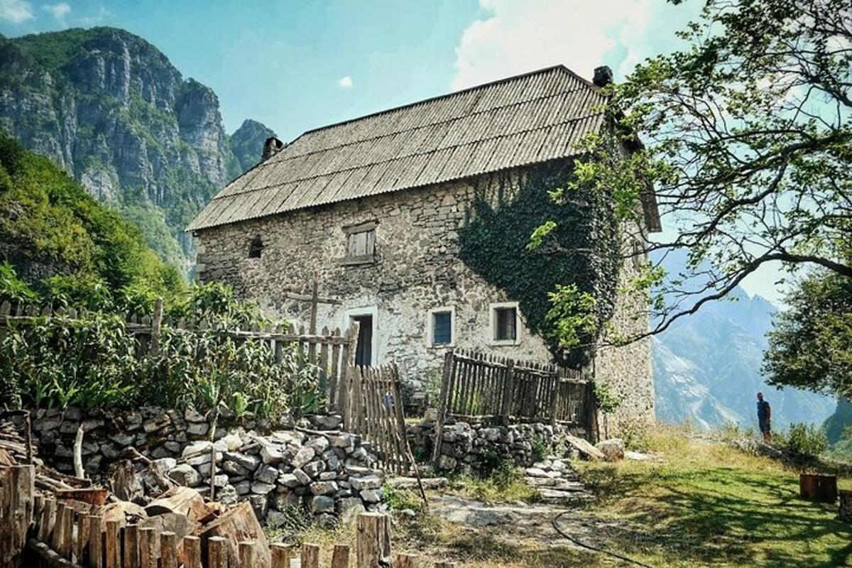 una antiga casa de pedra a les muntanyes amb una tanca