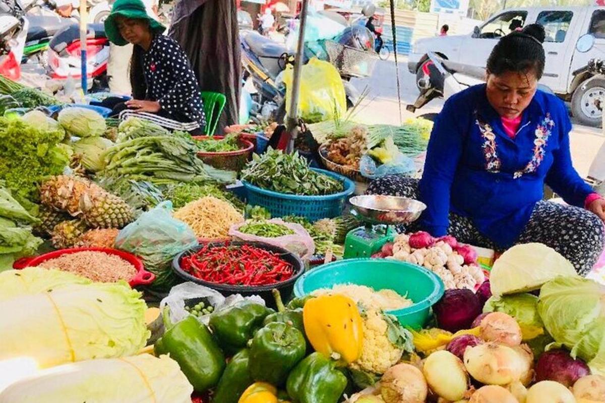 una dona asseguda davant d'un mercat amb verdures