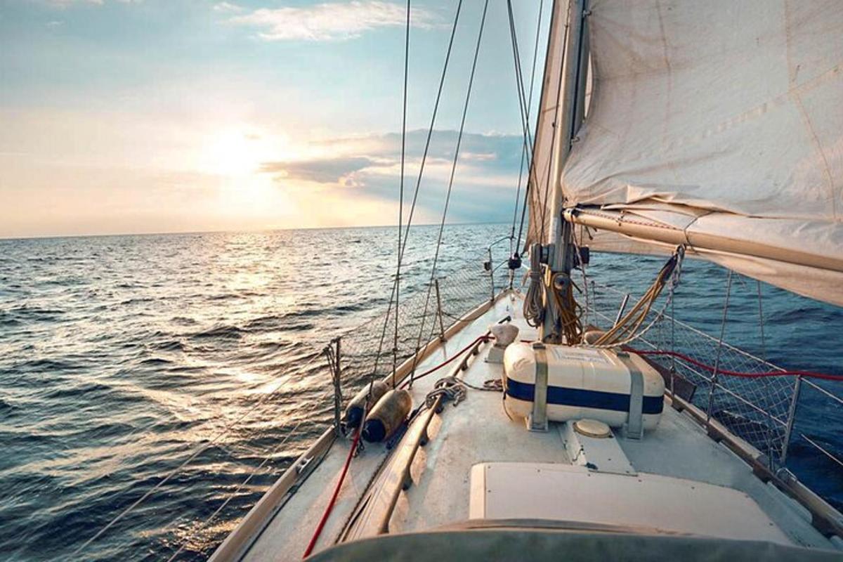 a sail boat in the ocean with the sun setting