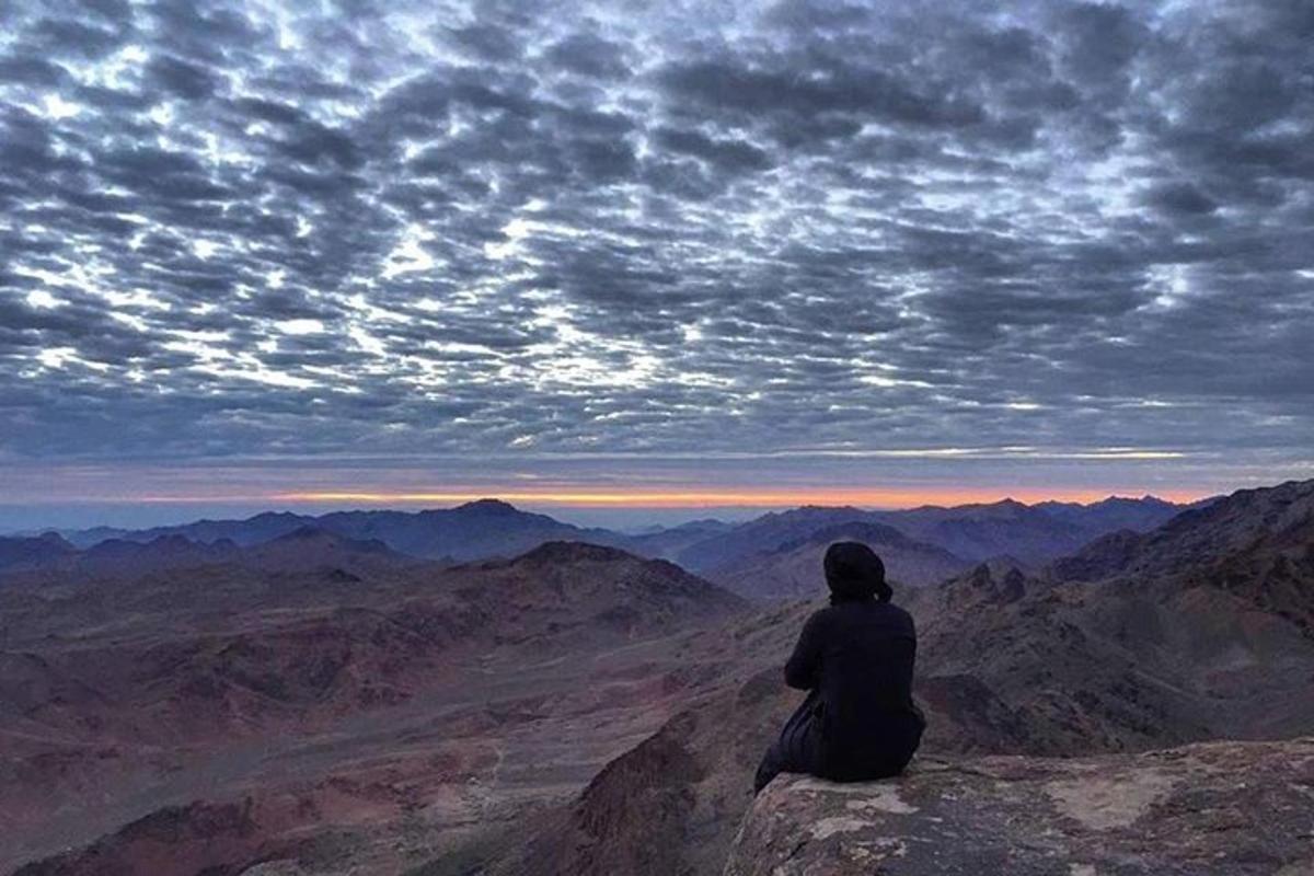 una persona sentada en la cima de una montaña mirando al cielo