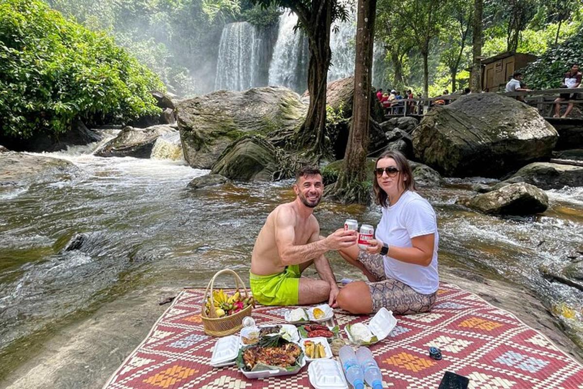 isang lalaki at babae na nakaupo sa isang picnic blanket sa tabi ng isang talon
