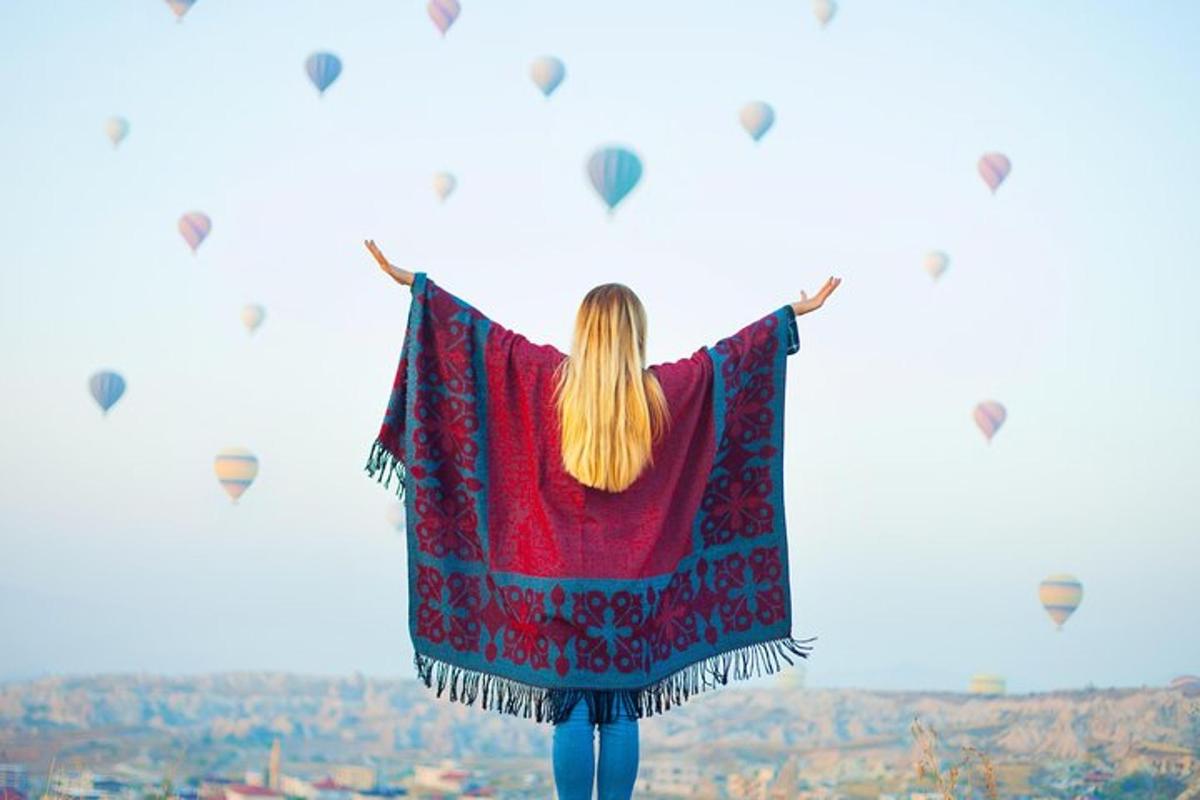 o femeie care stă pe vârful unui deal cu baloane cu aer cald