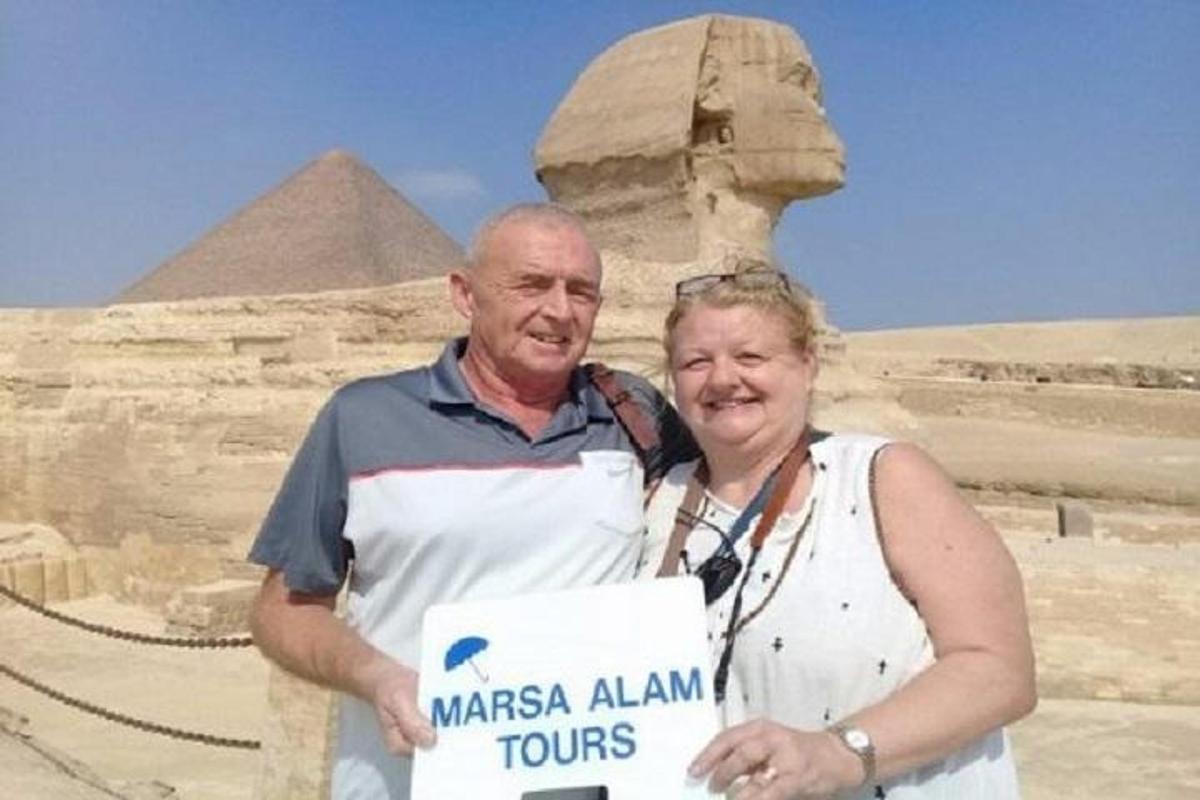 a man and woman holding a sign in front of the pyramids