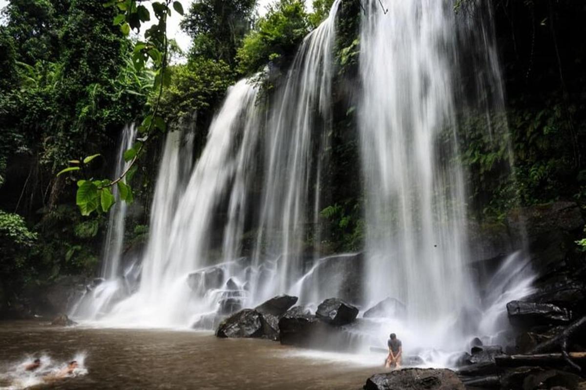 a person standing in the water in front of a waterfall